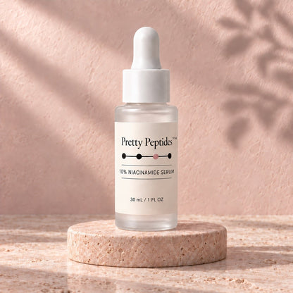 Pretty Peptides 10% Niacinamide Serum, 30 ml frosted dropper bottle on a travertine riser against a blush plaster wall