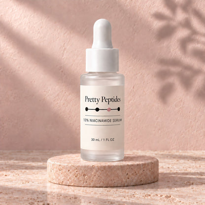 Pretty Peptides 10% Niacinamide Serum, 30 ml frosted dropper bottle on a travertine riser against a blush plaster wall